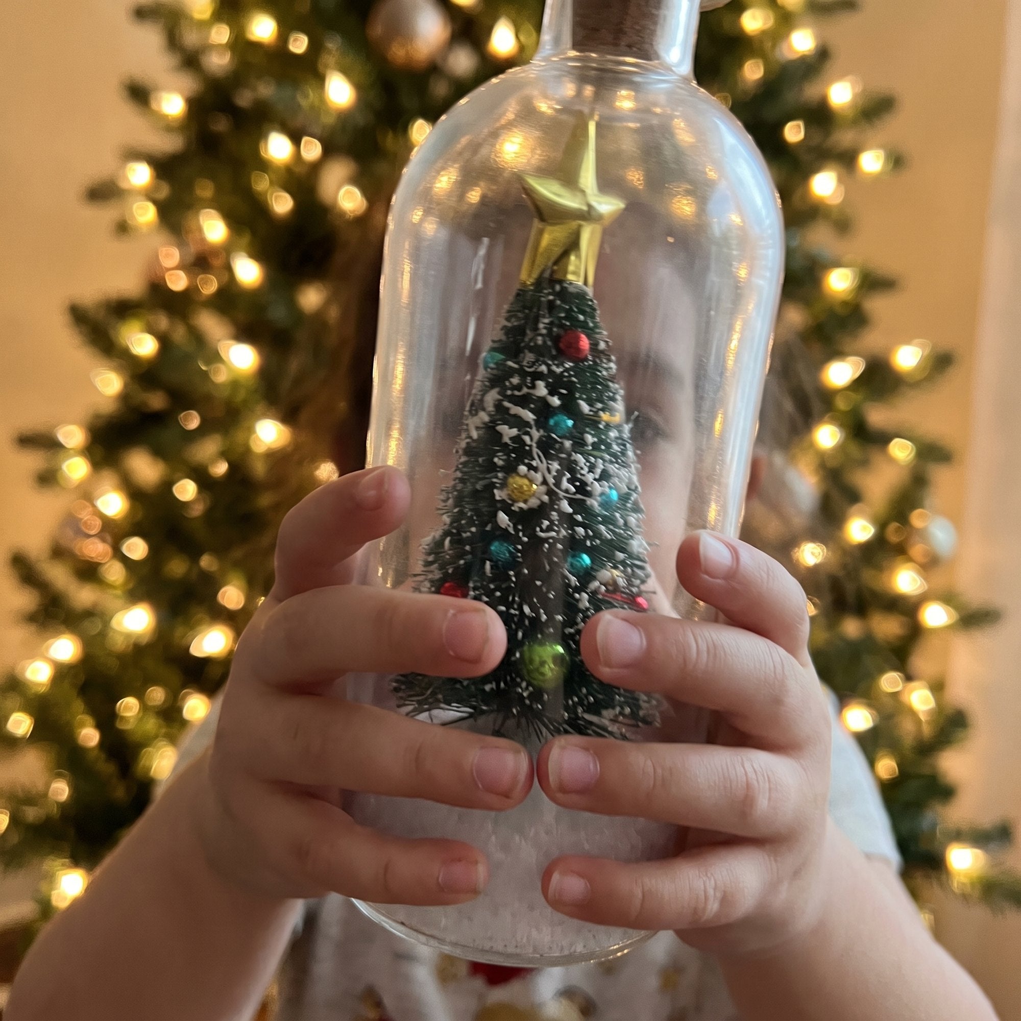 Hands holding the glowing Christmas tree bottle by the tree