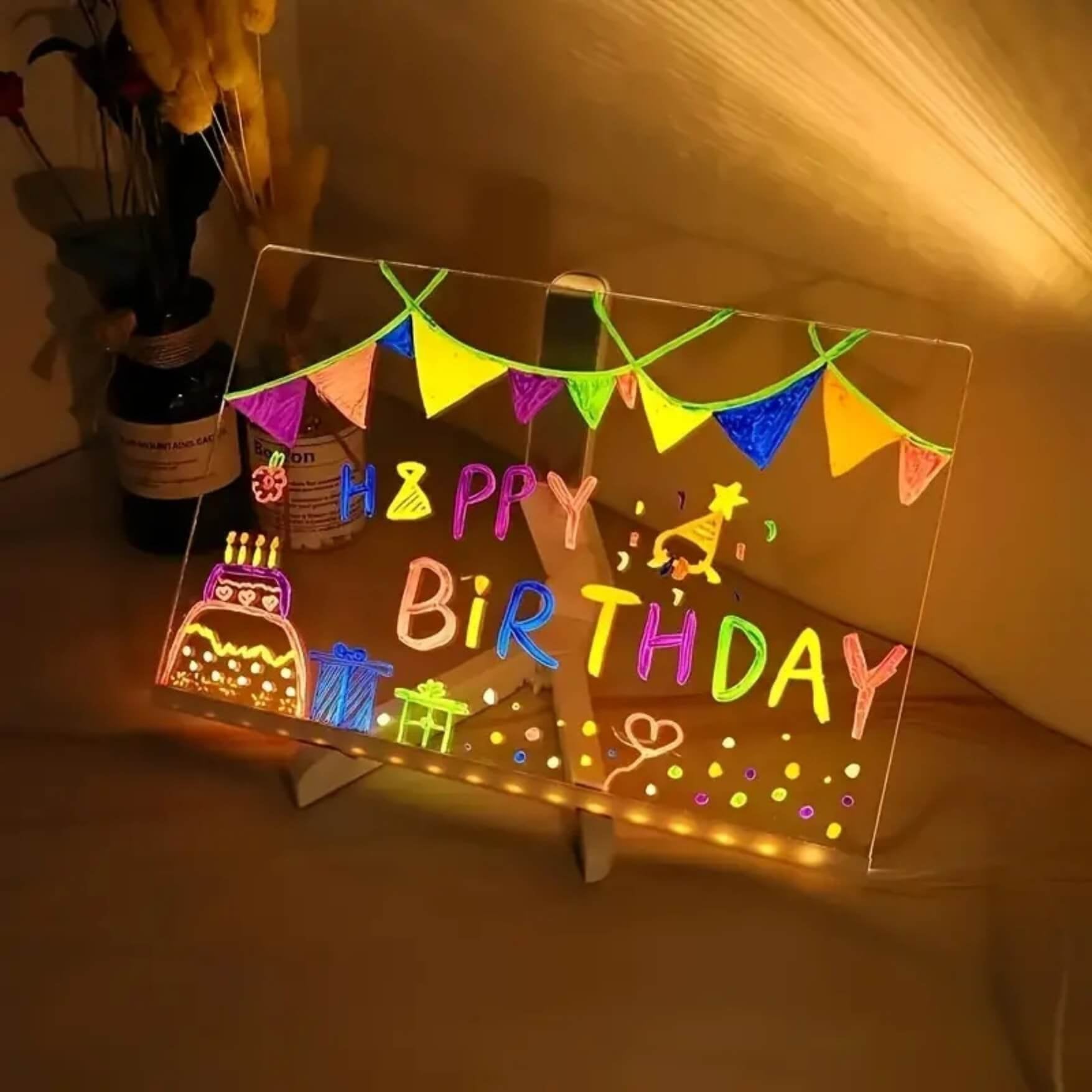 LED drawing board with glowing Happy Birthday message beside a cake
